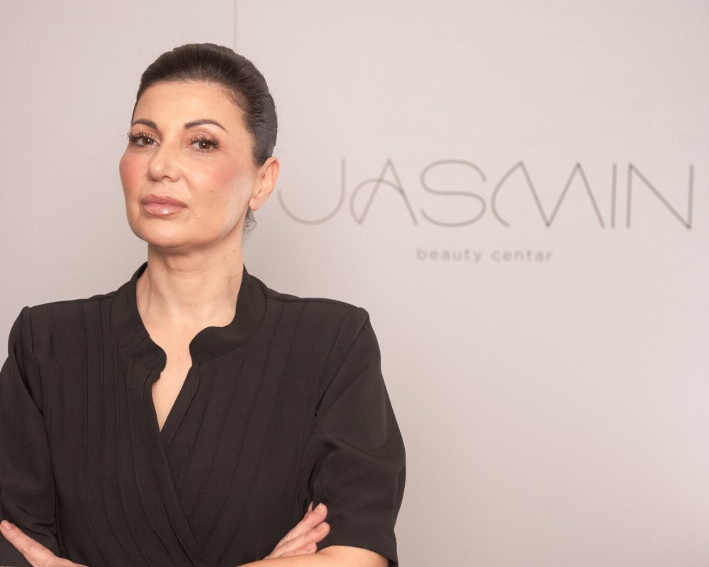 Profesionalni portret kozmetičarke u crnoj uniformi ispred logoa Jasmin beauty centar.
